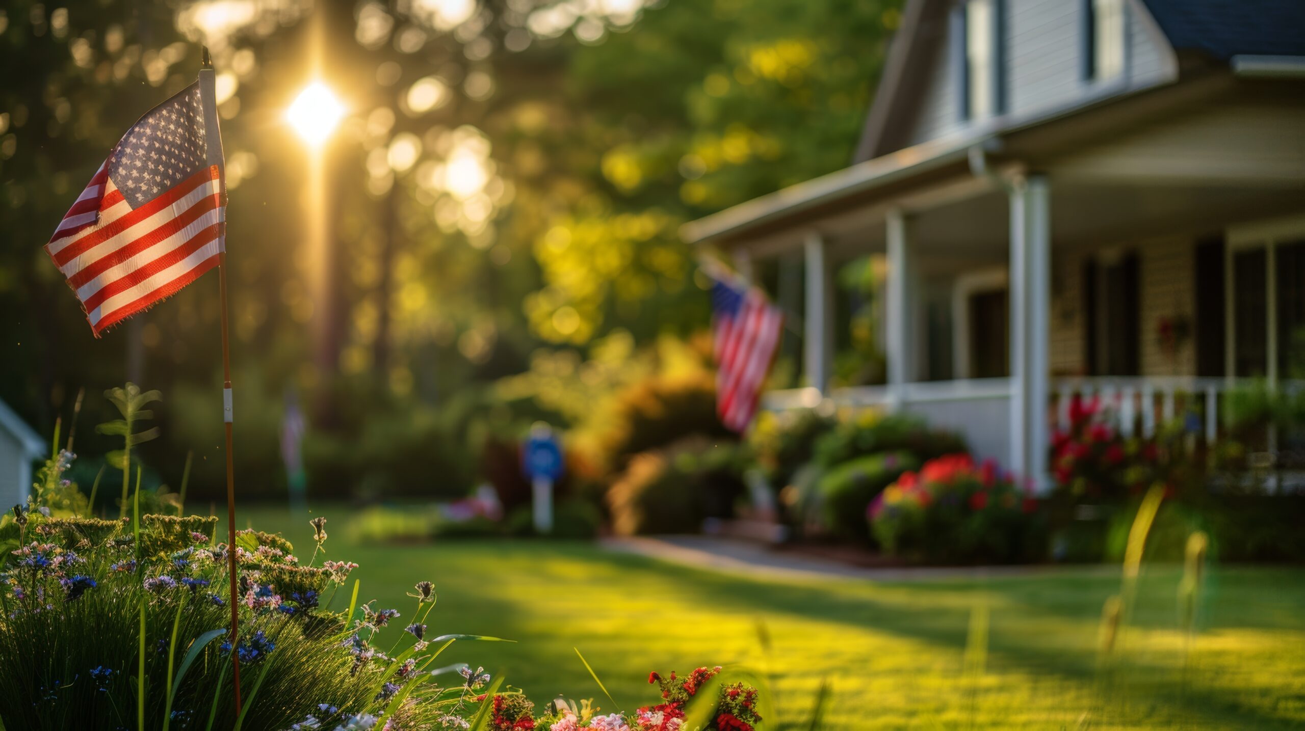 The American flag is flying on a corner of a residential house with a blurred background in the sunny afternoon